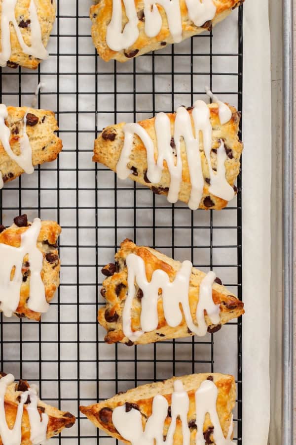 Made with simple ingredients, these Chocolate Chip Scones are perfectly flaky, soft, and buttery, with lots of melty chocolate chips! Baked scones on a wire cooling rack are drizzled with icing.