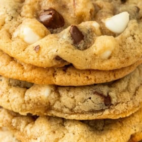 A close-up of a stack of chocolate chip walnut cookies, showing golden-brown edges, chocolate chips, and white chocolate chunks.