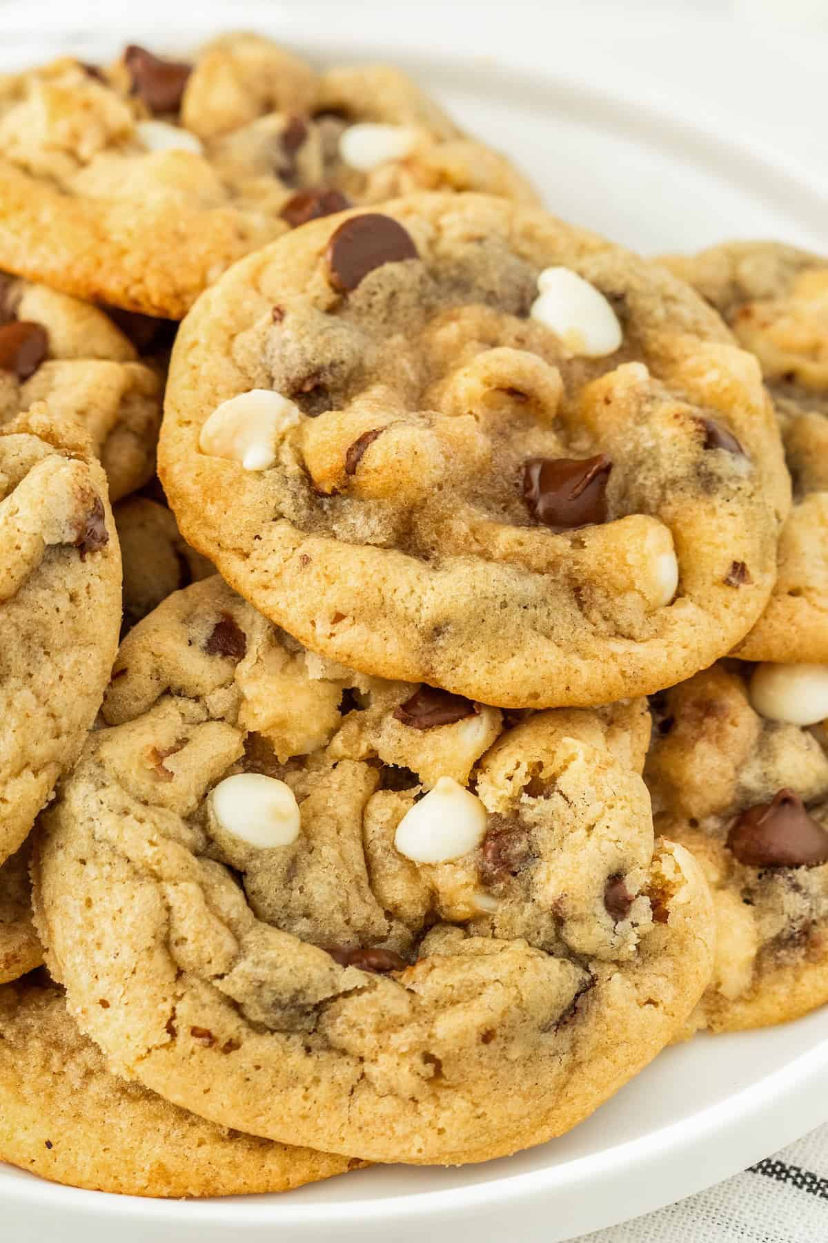 These soft and chewy Chocolate Chip Walnut Cookies have the perfect balance between sweet and nutty with two kinds of chocolate chips. A close-up of a plate piled with freshly baked chocolate chip walnut cookies, featuring both white and dark chocolate chips, on a white background.