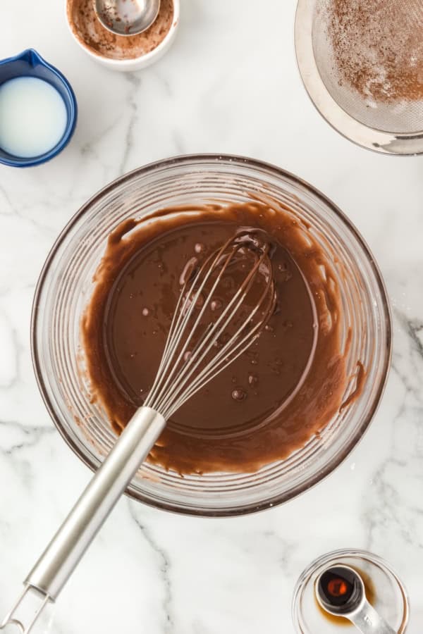 Chocolate donut glaze is being whisked in a large glass bowl.