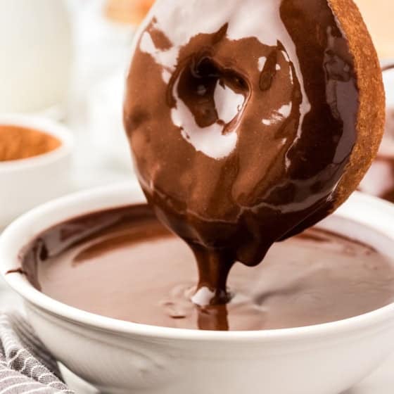 A donut is being dipped into a bowl filled with glossy chocolate glaze.