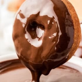 Donut is being dipped into rich chocolate glaze.