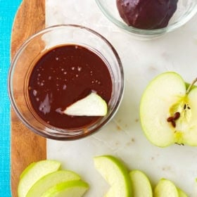Apple slices placed next to a bowl of rich chocolate glaze.