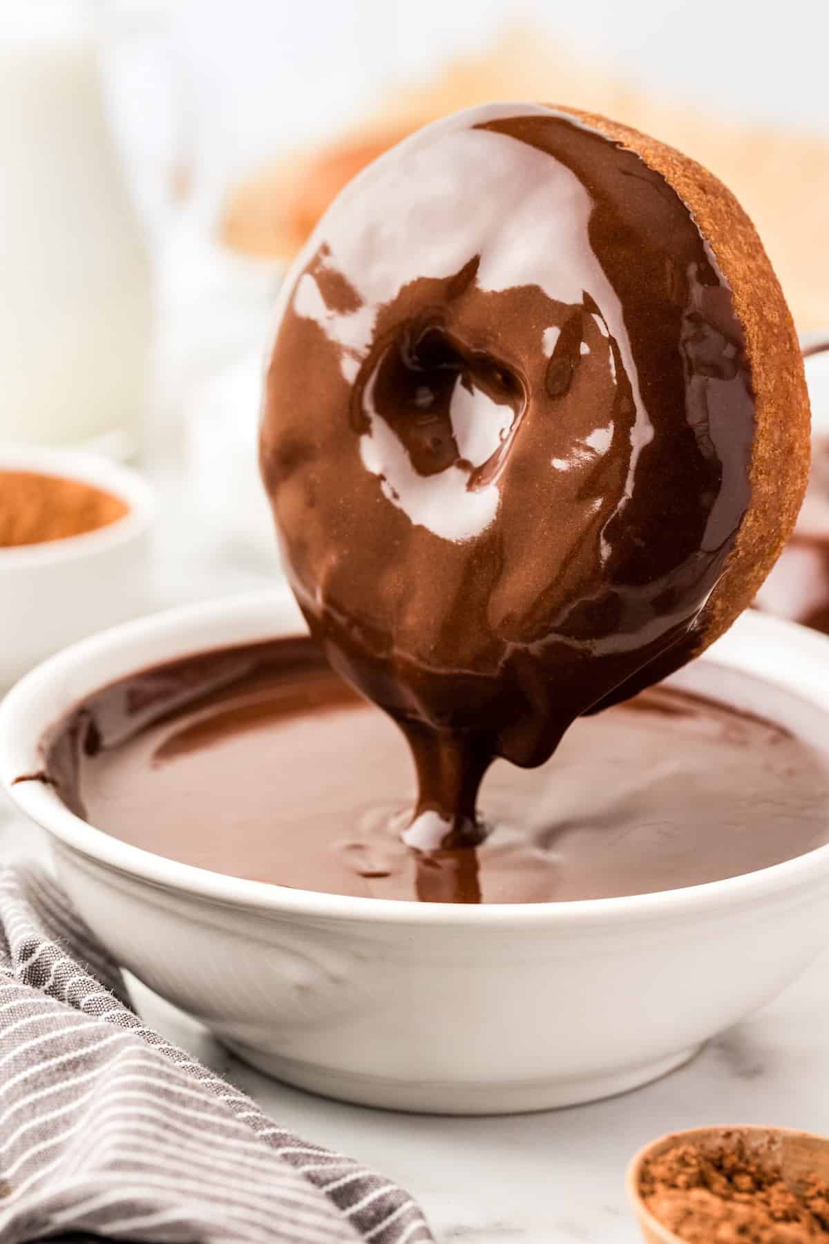 Perfectly rich and smooth, this easy Chocolate Glaze recipe is made with only 4 ingredients: powdered sugar, cocoa powder, milk and vanilla. A donut is being dipped into a bowl filled with glossy chocolate glaze.