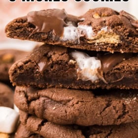 A stack of thick chocolate s’mores cookies with gooey melted chocolate and marshmallow filling is shown up close.