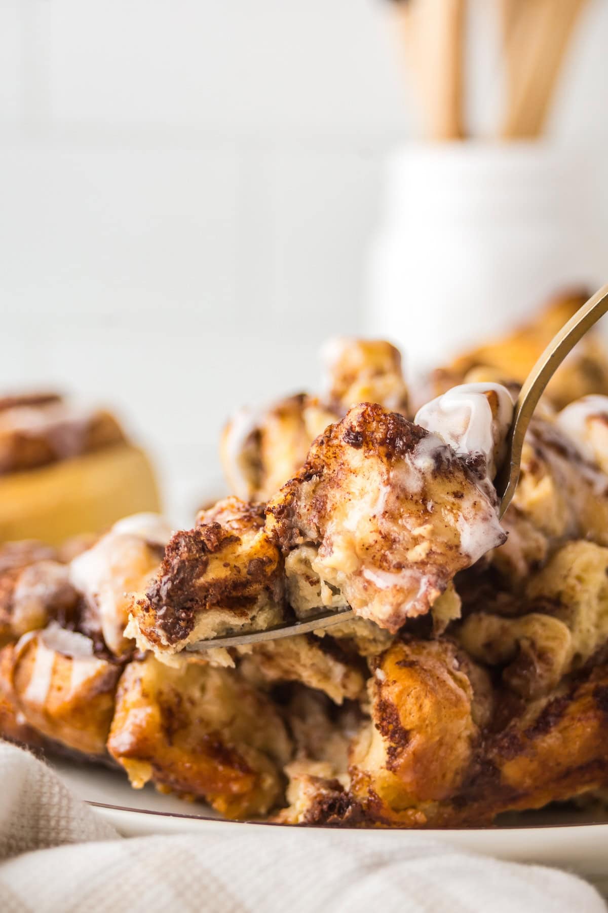Make easy with just 6-ingredients, every bite of this Cinnamon Roll Casserole tastes like the gooey and warm center of a cinnamon roll! A close-up of a fork lifting a piece of gooey cinnamon roll breakfast casserole topped with icing.