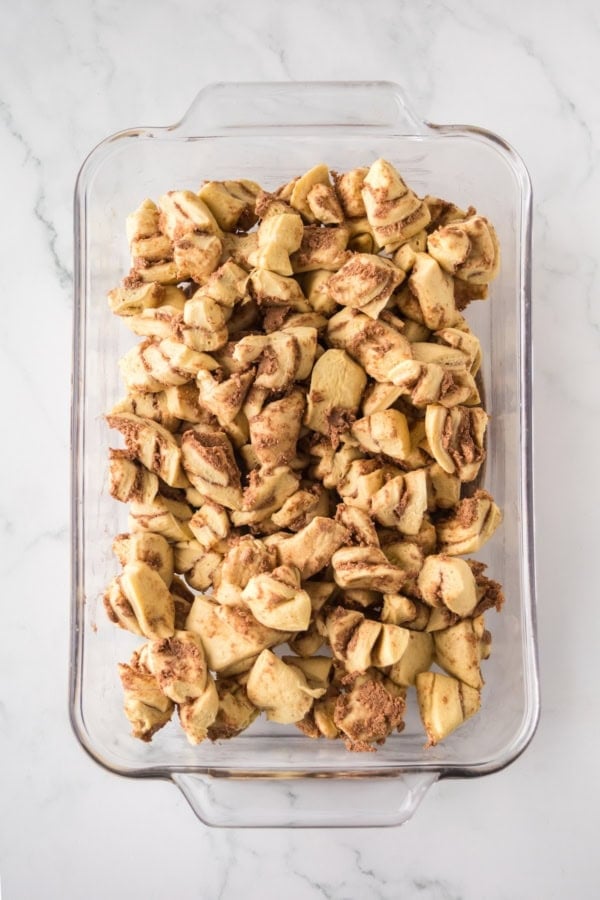 Make easy with just 6-ingredients, every bite of this Cinnamon Roll Casserole tastes like the gooey and warm center of a cinnamon roll! Glass casserole dish filled with uncooked cut pieces of cinnamon roll dough.