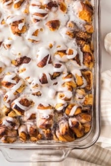 A close-up of a glass baking dish filled with cinnamon roll casserole drizzled with white icing.
