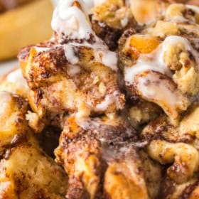 Close-up of a cinnamon roll casserole with swirls of icing on top. The dish looks gooey and soft with visible cinnamon and sugar layers.