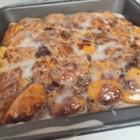 A close-up of a cinnamon roll breakfast casserole in a baking pan with a light glaze on top.