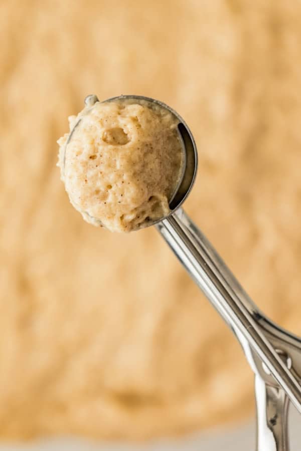 A cookie scoop is lifting a portion of sticky batter from the mixing bowl.