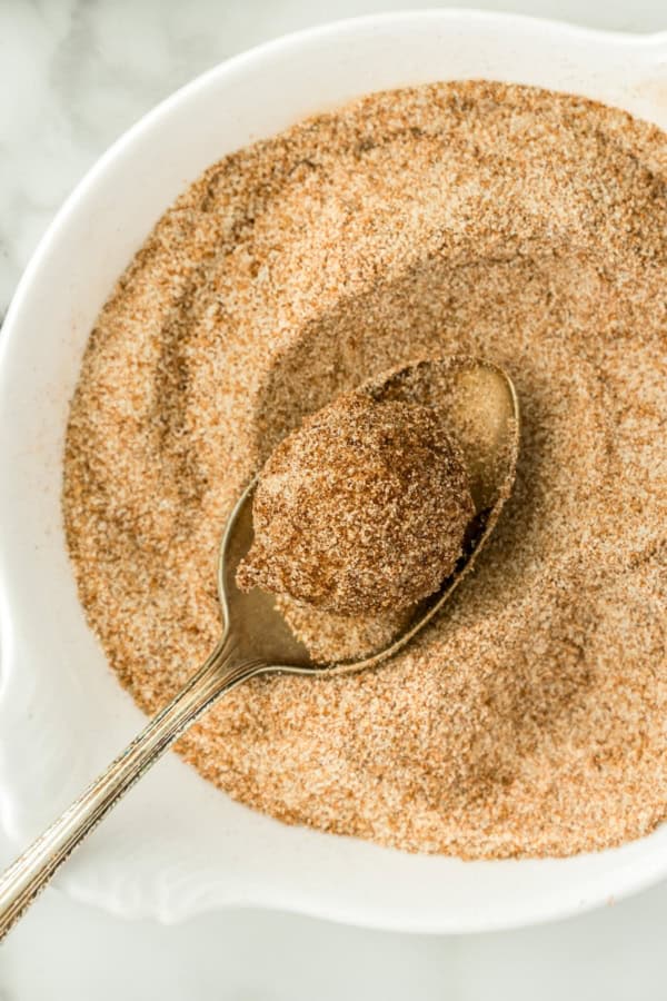 A hot donut hole is being coated in cinnamon sugar in a white bowl.