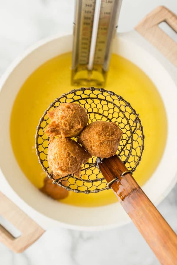 A wire scooper is lifting several freshly cooked donut holes from hot oil.