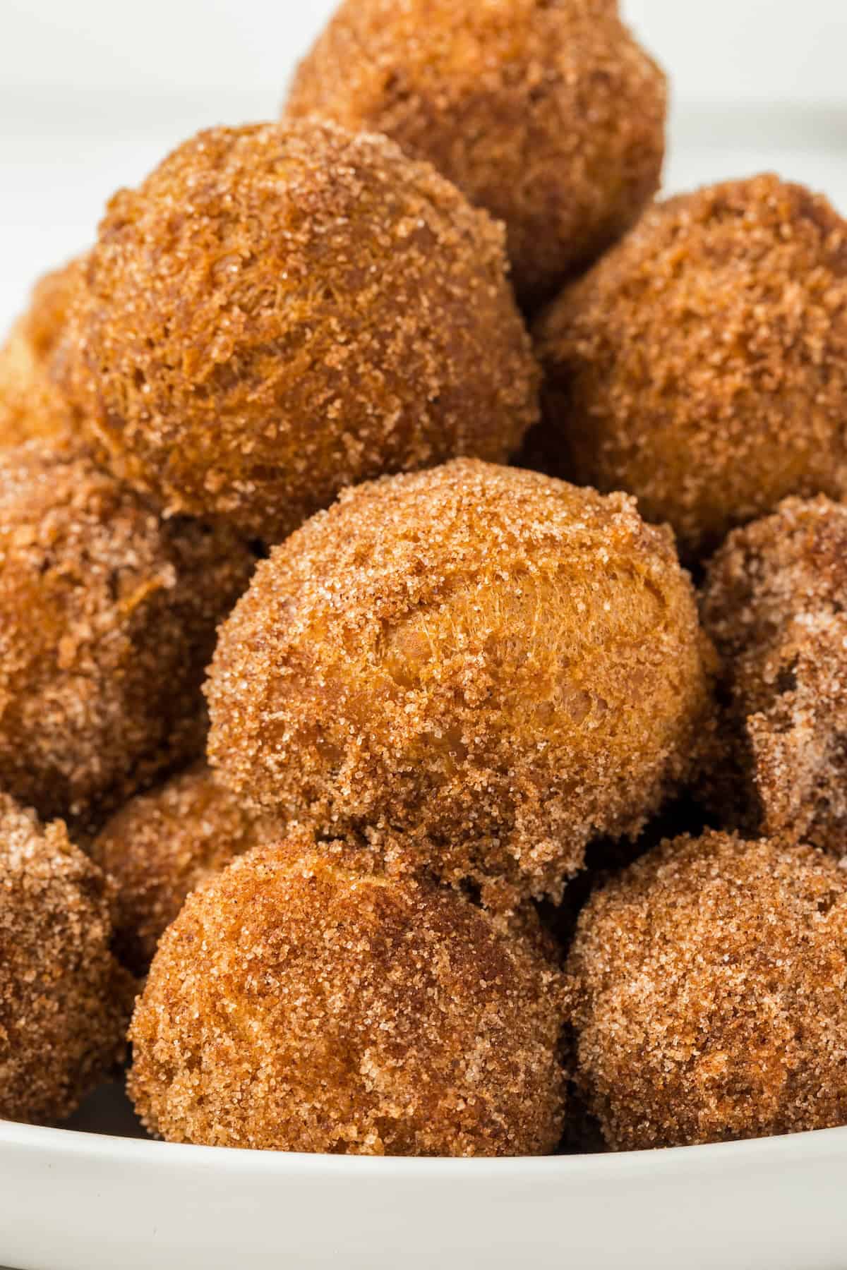 With a crispy outside and soft center, these Cinnamon Sugar Donut Holes are simple to make in 20-minutes — requiring no yeast or rising time! A batch of cinnamon sugar donut holes presented in a white bowl.