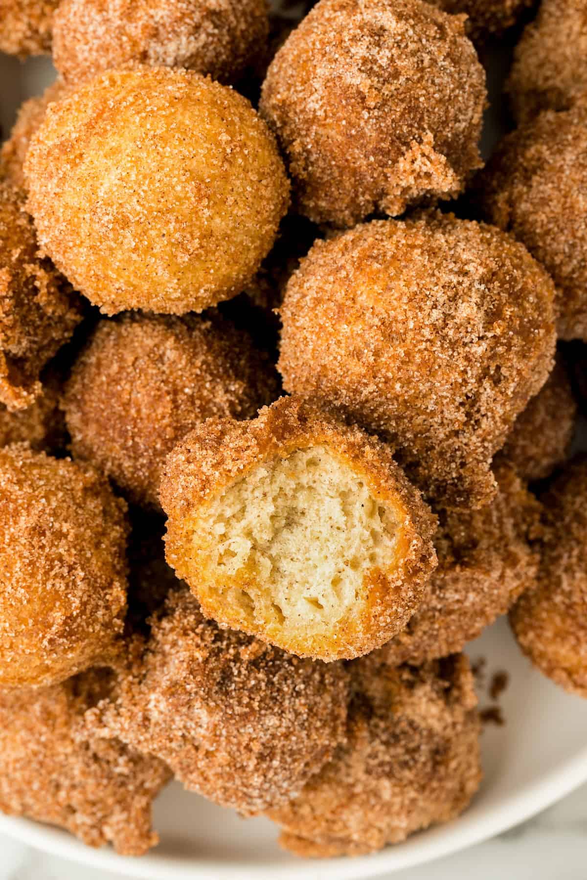 With a crispy outside and soft center, these Cinnamon Sugar Donut Holes are simple to make in 20-minutes — requiring no yeast or rising time! A single cinnamon sugar donut hole has been bitten into and placed back in the pile.