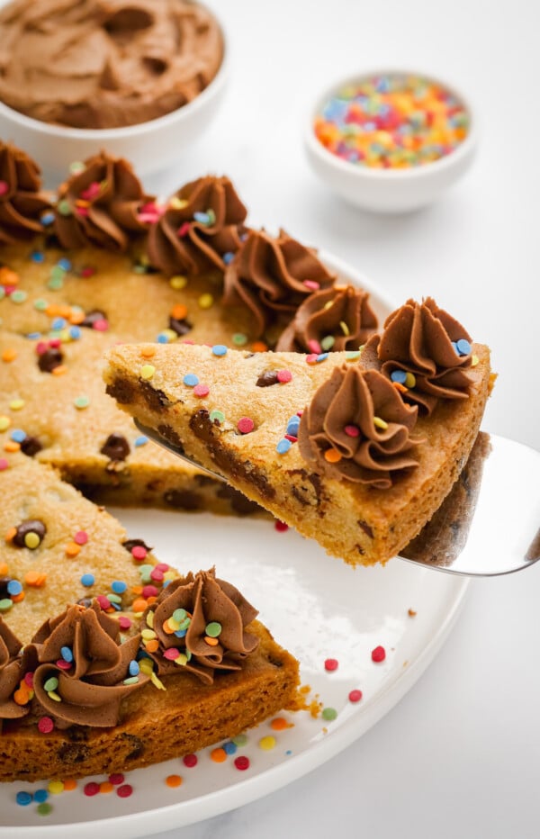 Slice of chocolate chip cookie cake with frosting.