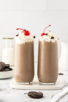 Two milkshakes, side by side, topped with whipped cream and cherries.