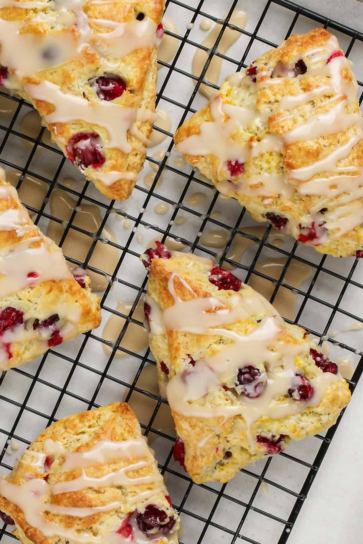 Perfectly dense and flaky, these Cranberry Orange Scones are filled with tart cranberries & fresh orange zest. Easy to make in under an hour! Glazed cranberry orange scones on a wire cooling rack.