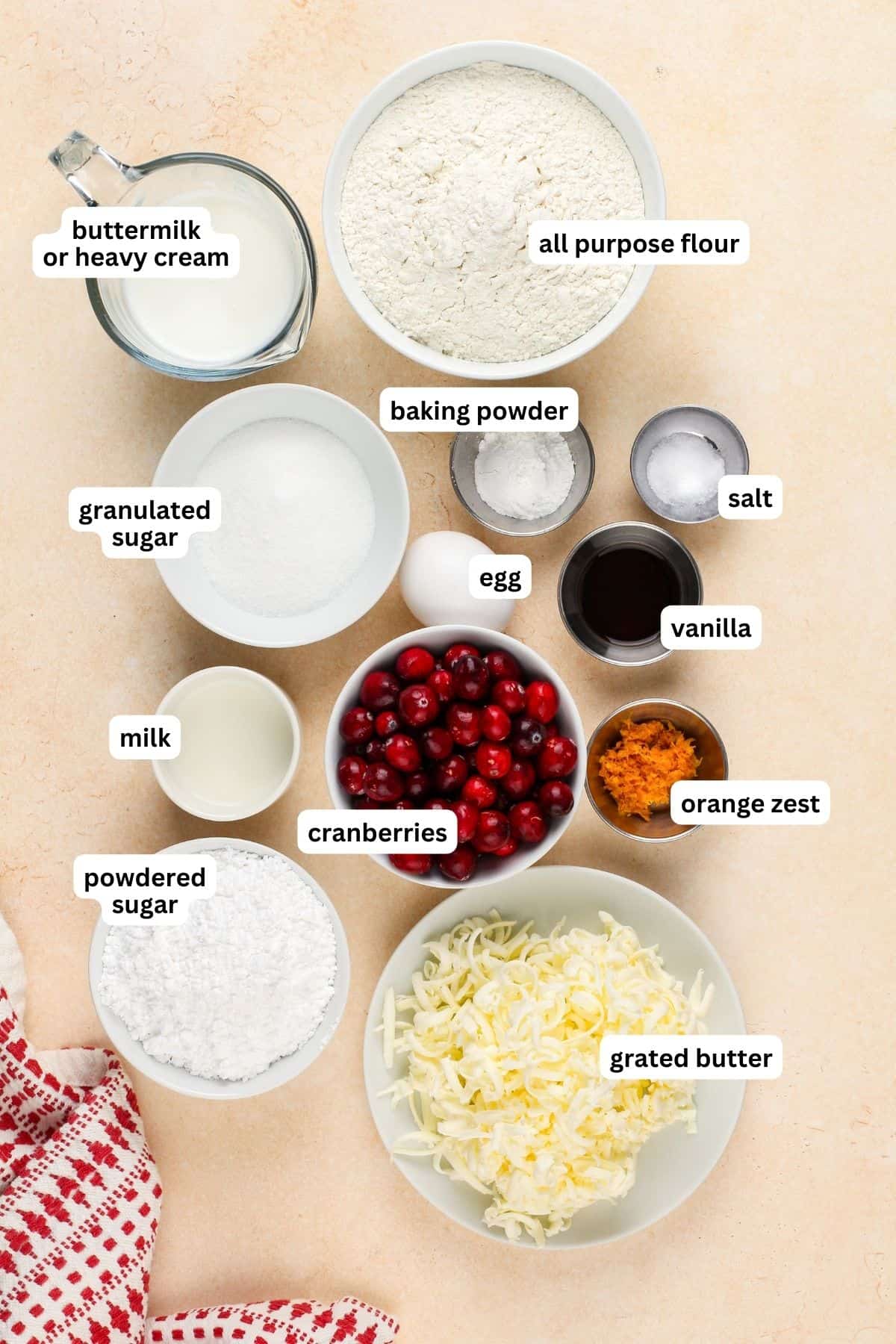 Perfectly dense and flaky, these Cranberry Orange Scones are filled with tart cranberries & fresh orange zest. Easy to make in under an hour! Ingredients for cranberry orange scones recipe in order from top to bottom: buttermilk or heavy cream, all purpose flour, granulated sugar, baking powder, salt, milk, cranberries, egg, vanilla, orange zest, powdered sugar, grated butter.