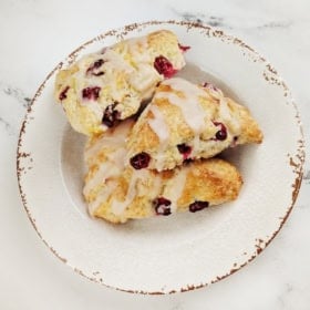 Three cranberry orange scones with sweet orange glaze on a plate.