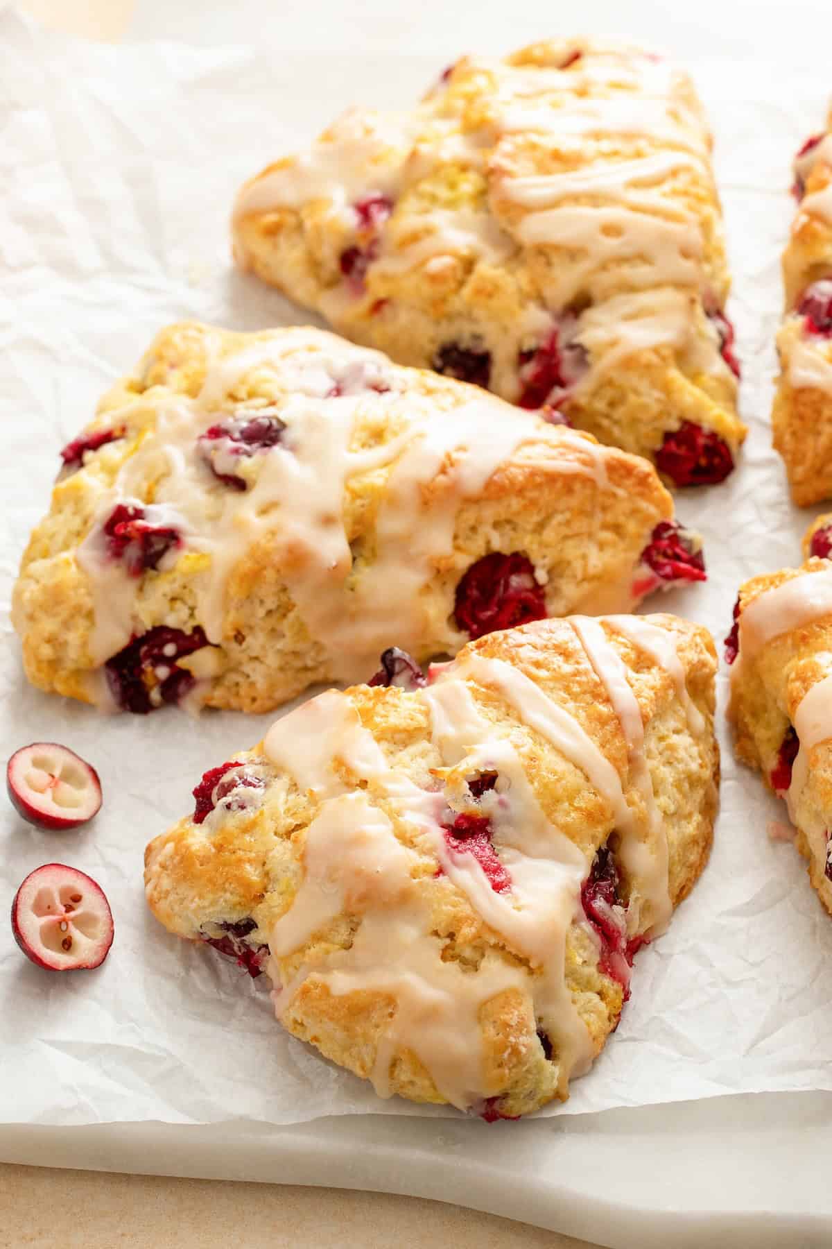 Perfectly dense and flaky, these Cranberry Orange Scones are filled with tart cranberries & fresh orange zest. Easy to make in under an hour! Fresh cranberries are scattered around several orange cranberry scones.