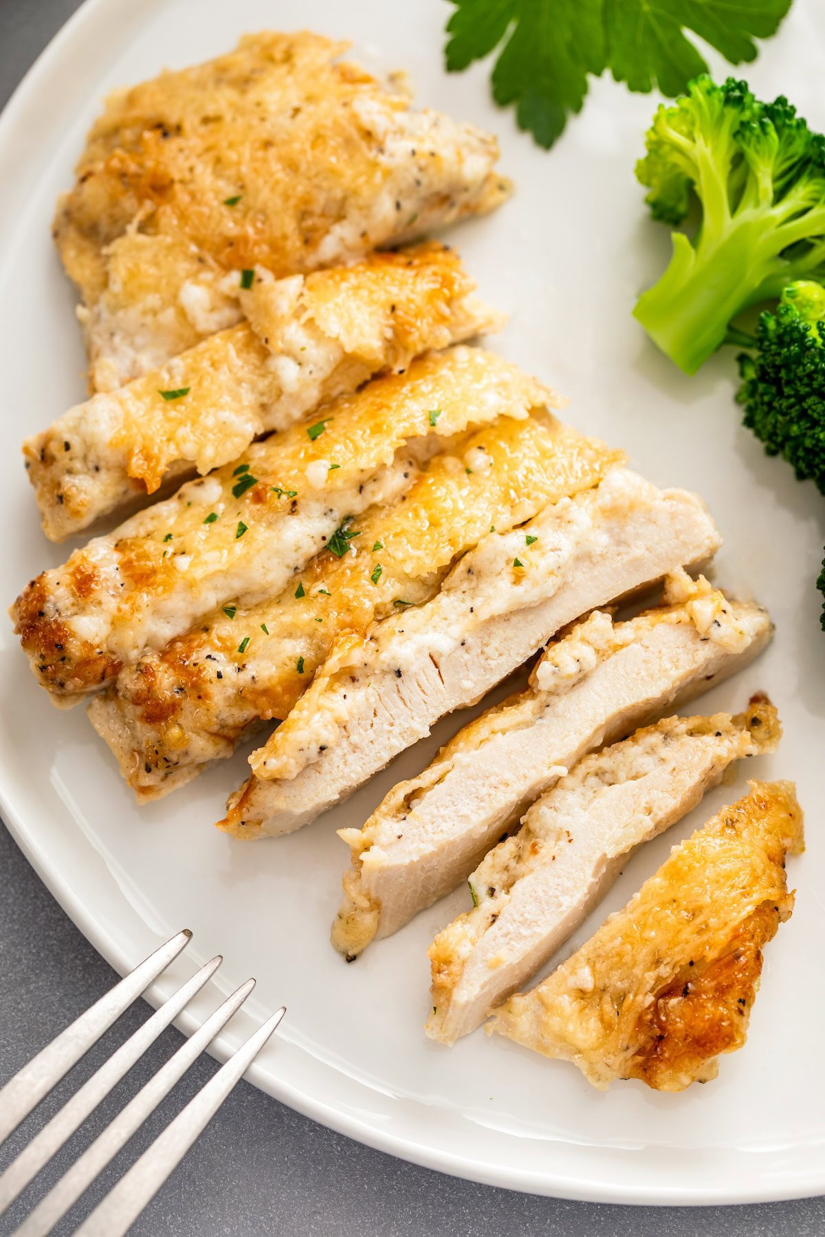 This creamy Garlic Parmesan Chicken recipe is a low-carb dinner that is packed with flavor, but made easy with just 4 simple ingredients! A sliced garlic parmesan chicken breast is presented on a white plate.