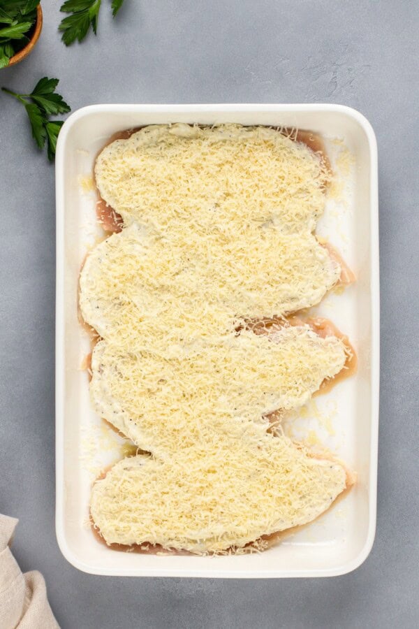 This creamy Garlic Parmesan Chicken recipe is a low-carb dinner that is packed with flavor, but made easy with just 4 simple ingredients! Raw chicken breasts are topped evenly with a mayo mixture and parmesan cheese in a baking dish.