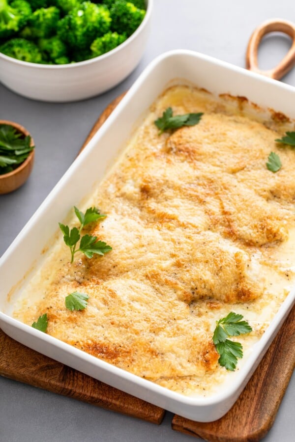 This creamy Garlic Parmesan Chicken recipe is a low-carb dinner that is packed with flavor, but made easy with just 4 simple ingredients! Green parsley garnished a baking dish filled with baked parmesan chicken.