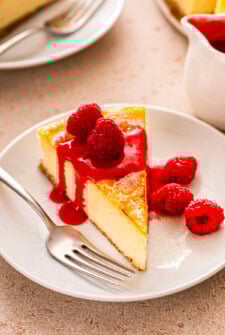 Slice of creme brulee cheesecake with fresh raspberries and fruity raspberry sauce on top.