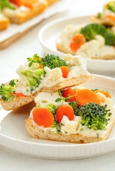 Two square pieces of fresh veggie pizza with crescent rolls stacked on a white plate.