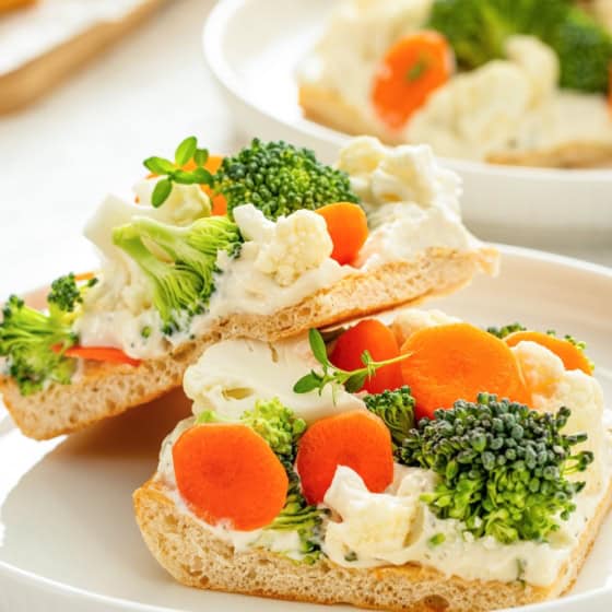 Two square pieces of fresh veggie pizza with crescent rolls stacked on a white plate.