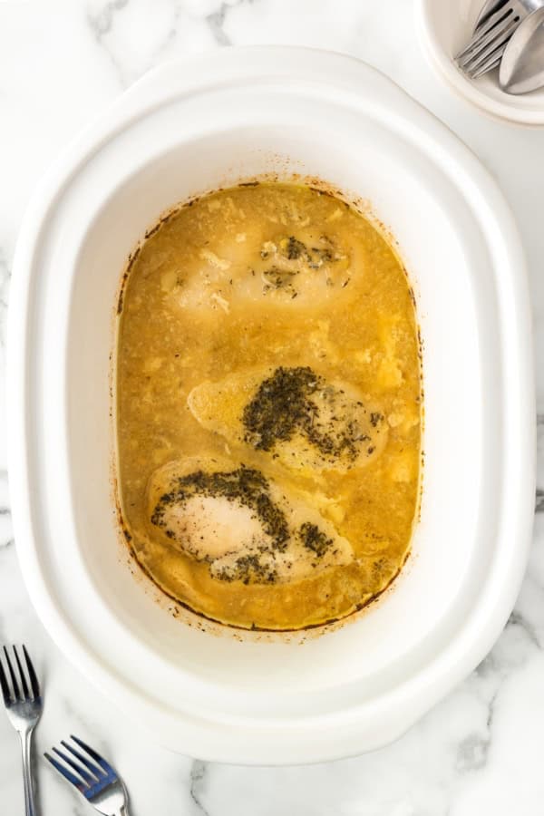 Skip the canned soup! This easy Crockpot Chicken and Gravy recipe is made from scratch - just real ingredients, creamy gravy, and big flavor! Three seasoned chicken breasts cooked in a creamy gravy inside a white slow cooker, viewed from above, with two forks on the side.