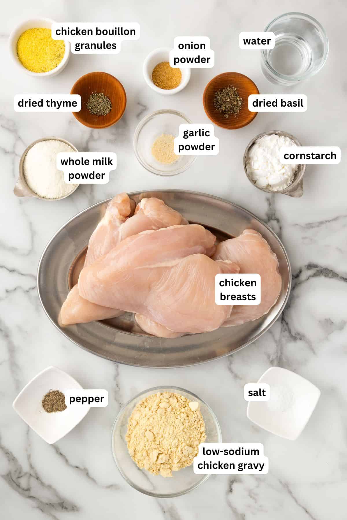 Skip the canned soup! This easy Crockpot Chicken and Gravy recipe is made from scratch - just real ingredients, creamy gravy, and big flavor! Ingredients for a crockpot chicken and gravy recipe arranged on a marble surface, including raw chicken breasts, spices, corn starch, milk powder, chicken gravy mix, water, and seasonings in small bowls, each labeled with text.