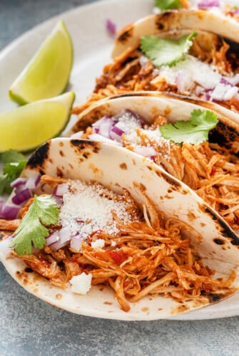 Close up shot of chicken tacos on a plate, topped with cheese and other toppings.