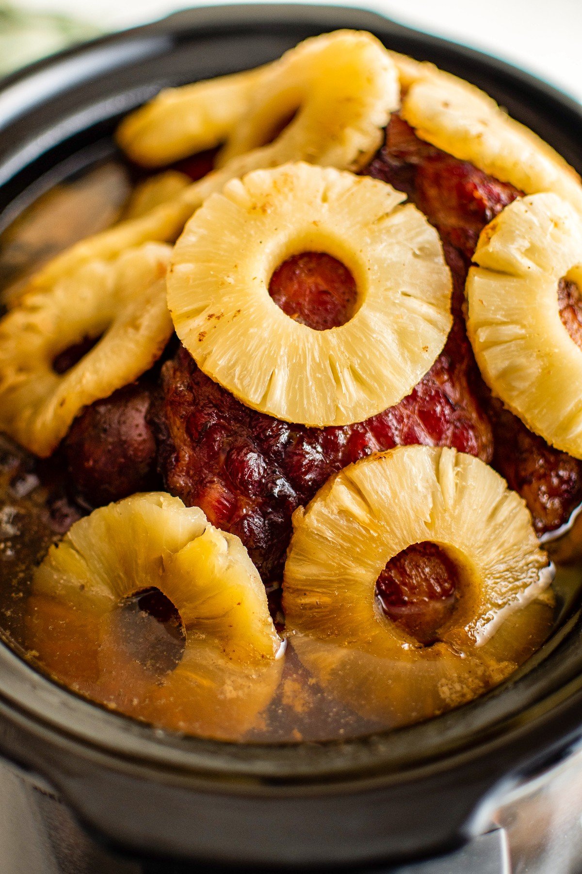 Save oven space with this easy crockpot ham recipe, slow-cooked to juicy perfection in a quick homemade brown sugar and pineapple glaze. Pineapple slices are placed all over a cooked ham.
