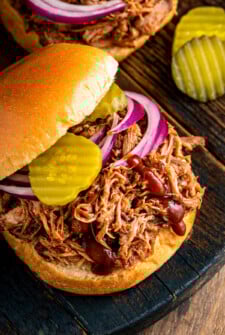 A slow cooker pulled pork sandwich topped with red onions, pickles and a drizzle of bbq sauce.