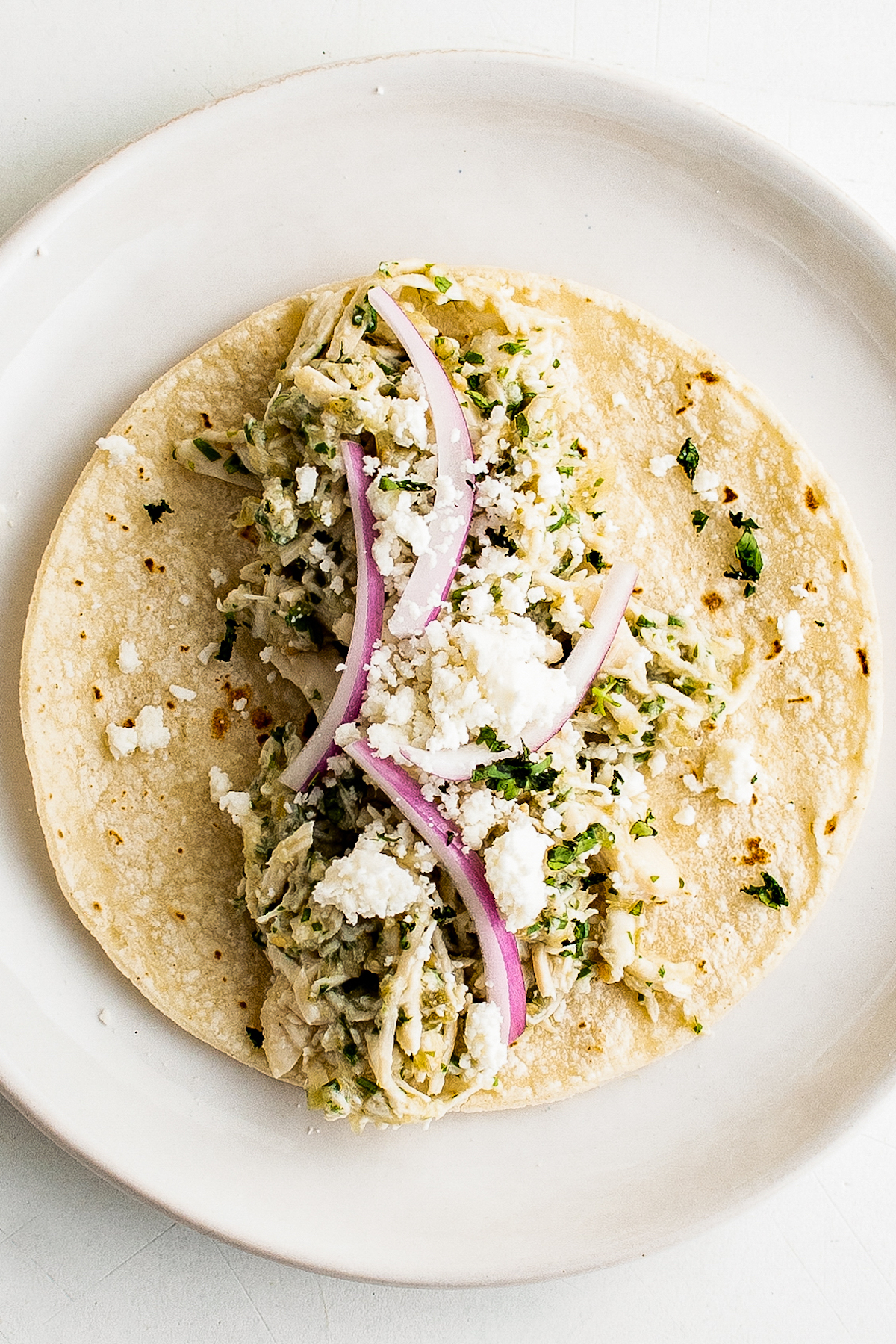 Crockpot Salsa Verde Chicken Tacos are an easy Taco Tuesday recipe! Made with tangy, savory salsa verde, they're bold, flavorful, and fun. A flour tortilla topped with shredded salsa verde chicken, red onion, and cotija cheese.