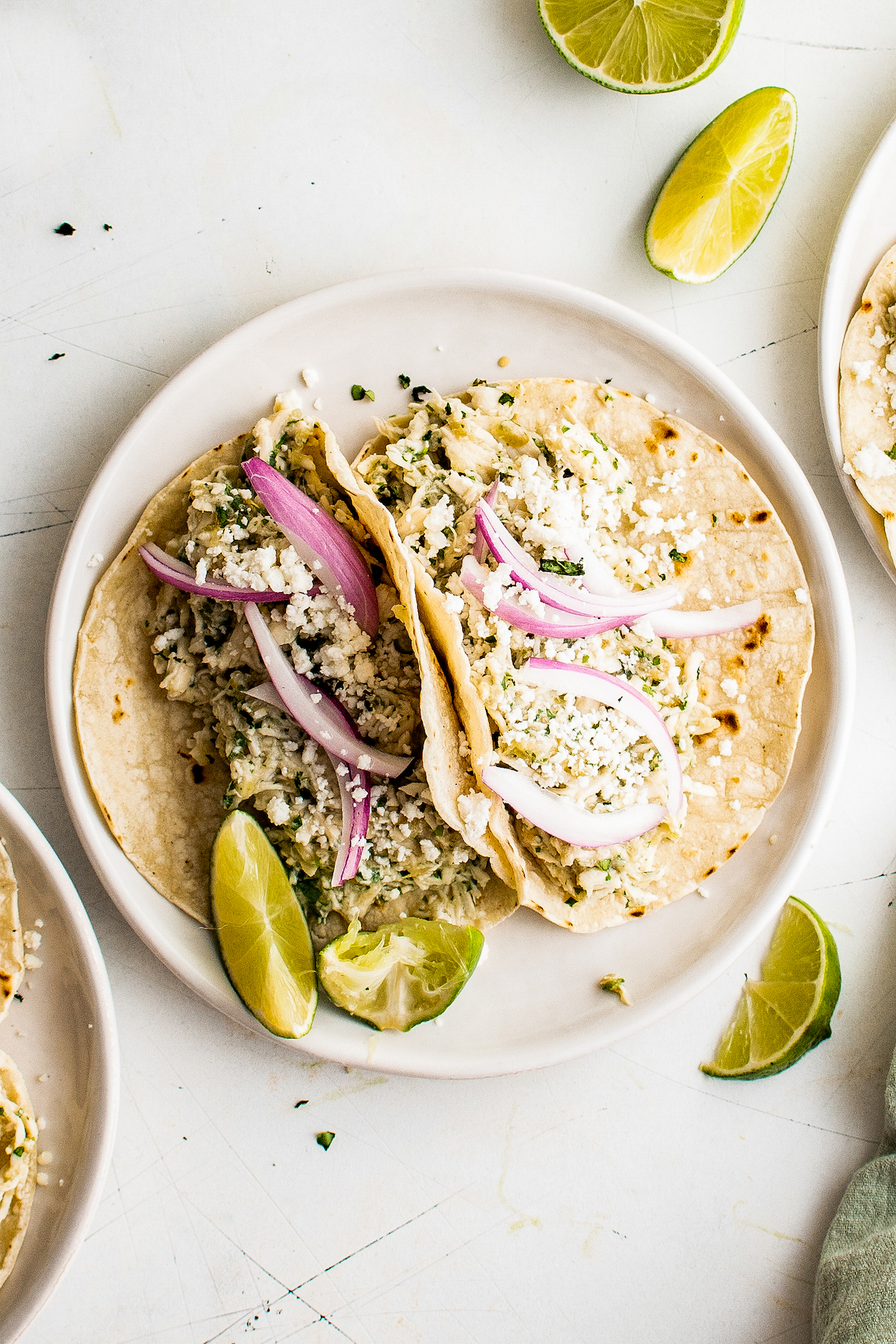 Salsa Verde Chicken Tacos in the Crockpot are an easy Taco Tuesday recipe! Made with tangy, savory salsa verde, these shredded chicken tacos will have everyone in the family fighting for the last one! Two salsa verde chicken tacos on a plate.
