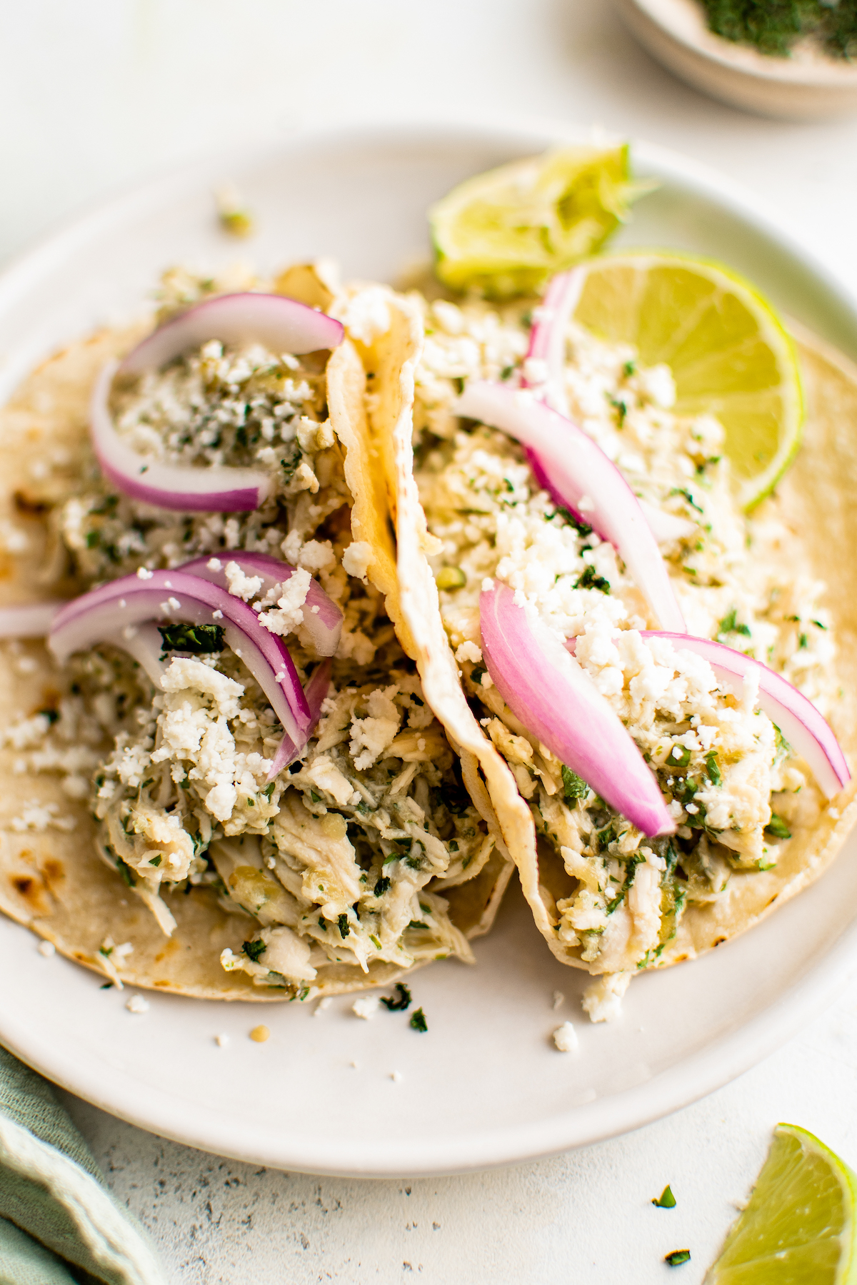 Salsa Verde Chicken Tacos in the Crockpot are an easy Taco Tuesday recipe! Made with tangy, savory salsa verde, these shredded chicken tacos will have everyone in the family fighting for the last one! Two shredded chicken tacos propped up against each other on a serving plate.