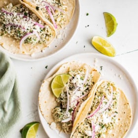 A crockpot filled with salsa verde chicken and two places of chicken tacos.