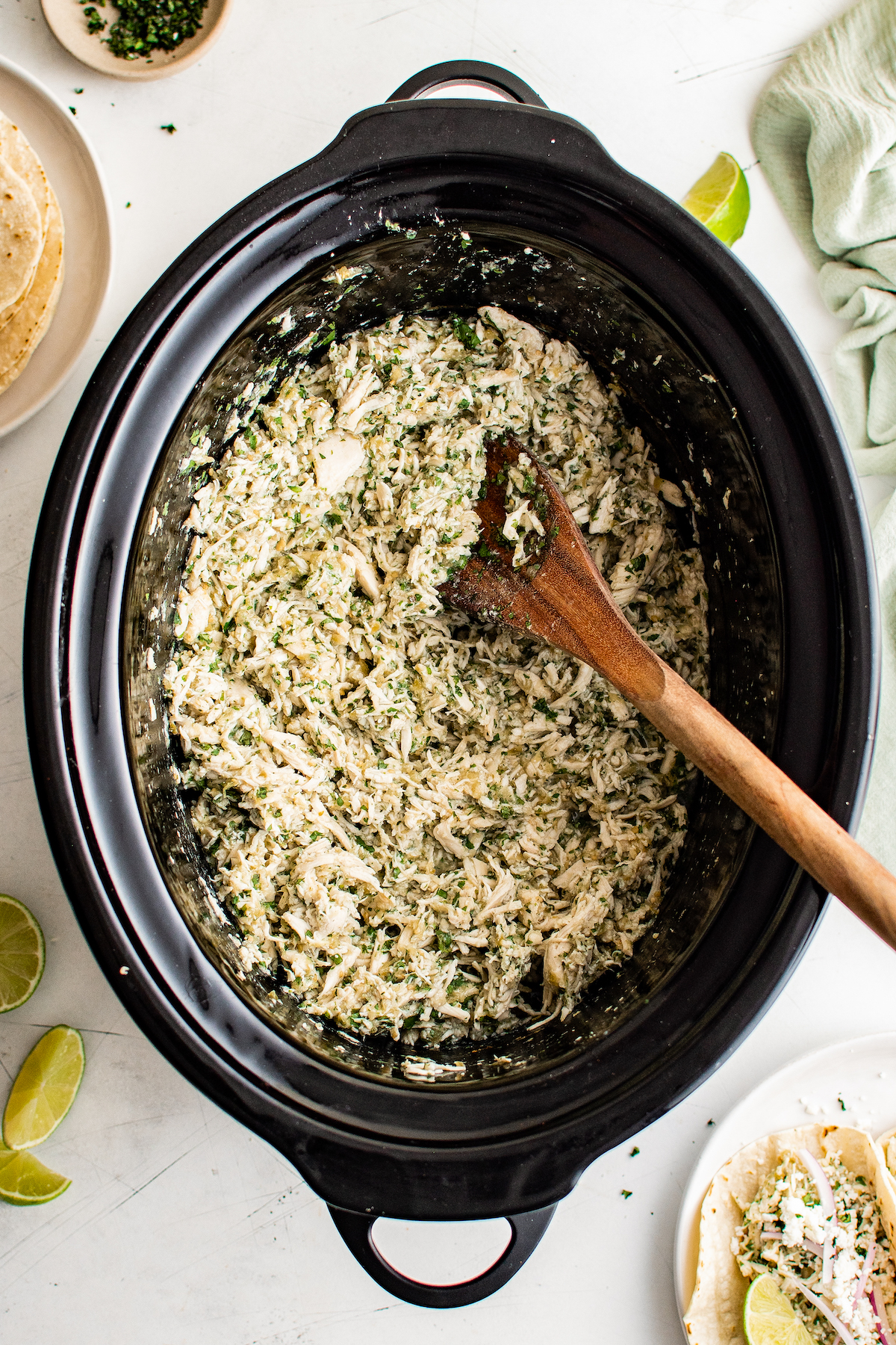 Crockpot Salsa Verde Chicken Tacos are an easy Taco Tuesday recipe! Made with tangy, savory salsa verde, they're bold, flavorful, and fun. Overhead shot of shredded chicken breast and green salsa being stirred together in a crockpot.