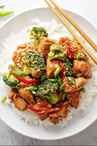 Crockpot Sesame Chicken with veggies and sesame seeds on a bed of rice on a white plate with chopsticks