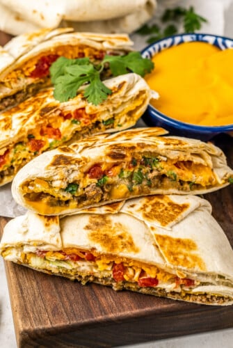 A Crunchwrap Supreme is golden, melty, and crunchy, sliced near a bowl of queso dip.
