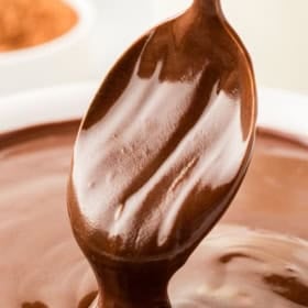 A spoon is dipping into thick, rich chocolate donut glaze.