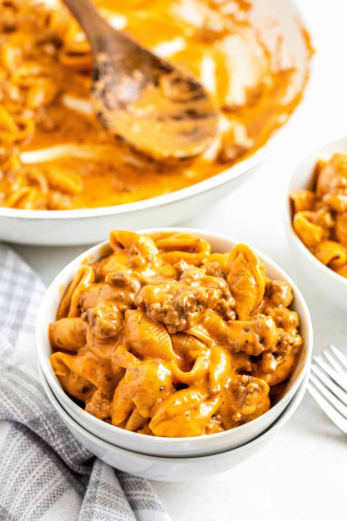 Ready in 30 minutes, this Homemade Hamburger Helper recipe is made with heavy cream and real cheddar cheese for an ultra-creamy sauce! A bowl of creamy cheeseburger hamburger helper with ground beef and an almost empty skillet in the background.