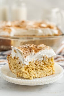 A square of cake on a small dessert plate. The baking dish with the rest of the cake is in the background of the shot.