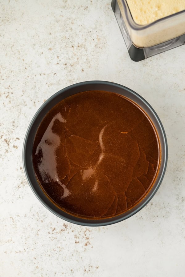 This festive Eggnog Flan is smooth, rich, and creamy, with plenty of nutmeg and rum for that classic spiced holiday flavor. A round baking pan filled with caramelized sugar with a blender full of a creamy flan mixture on the side.