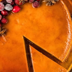 A golden eggnog Christmas flan with a slice removed, topped with sugared cranberries and star anise.
