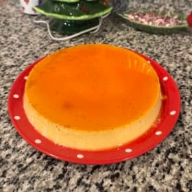 A creamy eggnog flan with glossy caramel top sits on a red plate.