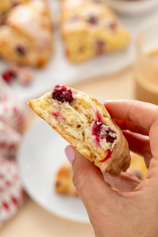 Perfectly dense and flaky, these Cranberry Orange Scones are filled with tart cranberries & fresh orange zest. Easy to make in under an hour! A single cranberry orange scone has been bitten into.